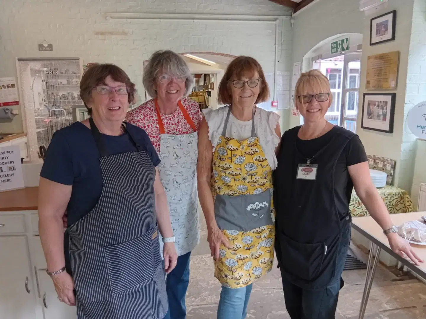 cafe team image A cosy cafe indoors with wooden chairs and tables, a stone floor and timbered roof.